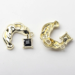 Macro shot of gold alloy C-shape pendant with lava texture and black square gemstone