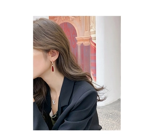 Détail de boucles d'oreilles rouges et collier lettre K argent sur un modèle