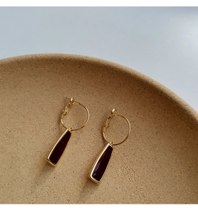 Vue macro de boucles d'oreilles créoles dorées avec pendentifs trapèzes rouge foncé