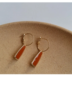 Détail de boucles d'oreilles rétro dorées avec pendentifs orange sur plateau céramique