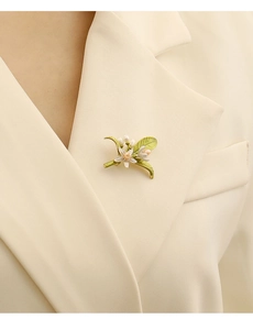 Dettaglio della spilla a fiore con perle indossata sul bavero di un blazer crema