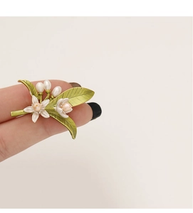 Dettaglio di elegante spilla a fiore bianco con perle e foglie su base dorata lucida