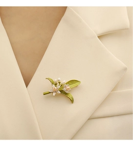Dettaglio spilla a foglia in smalto verde con fiore di perla su un bavero beige