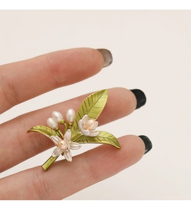 Dettaglio di una spilla floreale con foglie smaltate verdi, fiori bianchi e perle