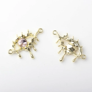 Macro shot of gold alloy eye pendant with pink rhinestone and hollow lava texture
