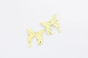 Macro detail of two light yellow alloy butterfly pendants with melted texture effect