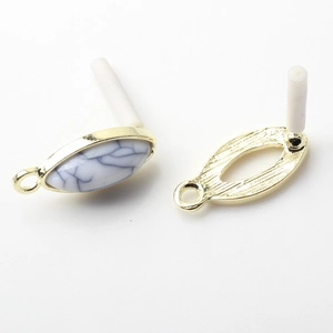 Macro detail of oval gold-plated earring connectors with white marble stone inlays