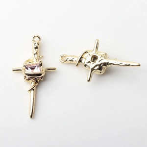 Detail of golden alloy cross pendants with center square pink gemstone and ornate texture