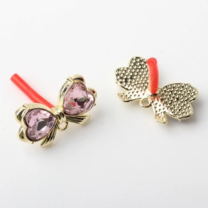 Detail of light gold bow earrings featuring pink heart-shaped crystals and hanging loops