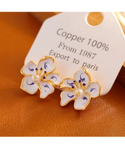 Detail of blue and white enamel flower earrings with a pearl center and gold-plated copper