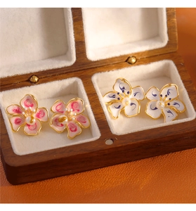 Detailed close-up of blue and pink enamel flower earrings in a wooden jewelry box