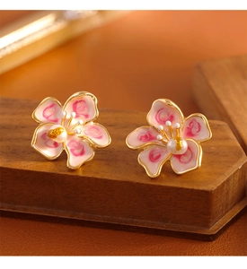 Detailed macro view of cherry blossom enamel stud earrings with central pearls on wood