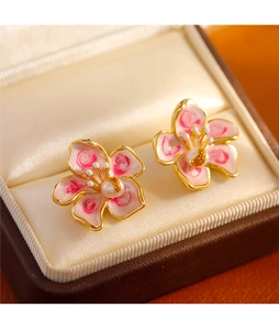 Macro view of pink cherry blossom enamel earrings with golden edges and pearl centers