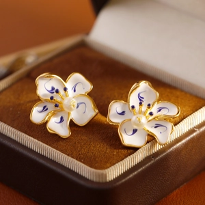 Blue and white enamel flower earrings with pearl centers and gold edges on velvet