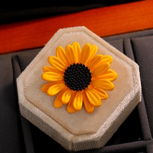 Exquise broche tournesol aux pétales jaunes et centre texturé noir sur un support à bijoux