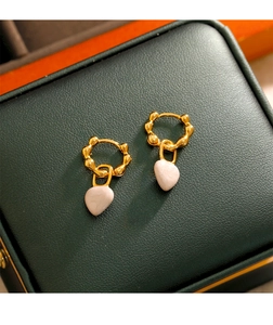 Détail de boucles d'oreilles cœur vintage dorées sur un coffret en cuir vert