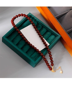 Détail du collier à perles rouges avec fermoir mousqueton doré et chaîne d'extension sur velours