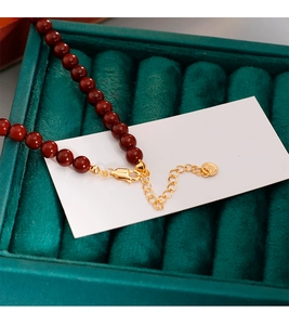 Gros plan du collier perlé rouge foncé avec fermoir doré et pendentif logo rond