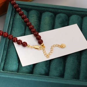 Collier minimaliste en perles rouge foncé avec fermoir doré sur écrin en velours vert