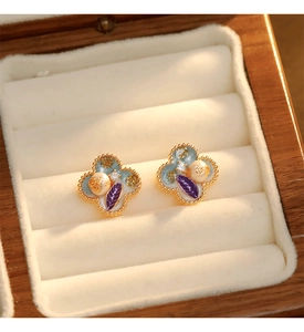 Détail de boucles d'oreilles trèfle en émail avec perle et pierre violette en boîte