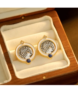 Close-up of vintage coin earrings with white enamel and blue gemstones in a wooden box