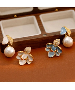 Détail de boucles d'oreilles émaillées fleurs avec perles et cristaux sur support bois