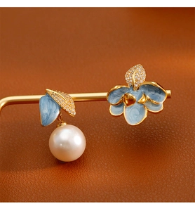 Détail de boucles d'oreilles fleurs en émail bleu asymétriques avec perles et zircons