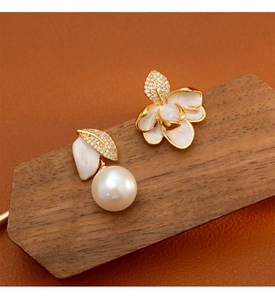 Détail de boucles d'oreilles asymétriques émaillées avec fleurs feuilles et perles blanches