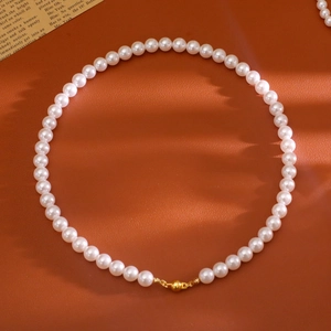 Gros plan d'un collier de perles blanches avec fermoir magnétique doré sur fond de cuir