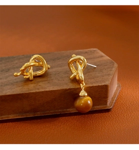 Gros plan de boucles d'oreilles dorées asymétriques avec nœud et perle en œil de tigre