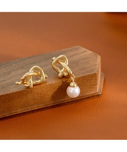 Détail de boucles d'oreilles torsadées dorées avec perle blanche sur cuir marron de luxe