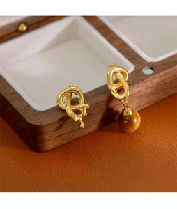 Gros plan de boucles d'oreilles dorées asymétriques avec perle œil de tigre sur bois