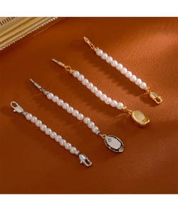 Détail de fermoirs mousquetons or et argent avec perles sur fond en cuir marron