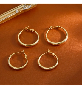 Gros plan de boucles d'oreilles créoles dorées en deux tailles sur cuir brun