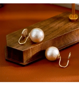 Gros plan de boucles d'oreilles perles blanc crème avec clips en métal doré et gravure