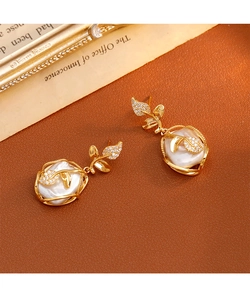 Detalle de pendientes de hoja con perlas barrocas y piedras sobre un fondo vintage