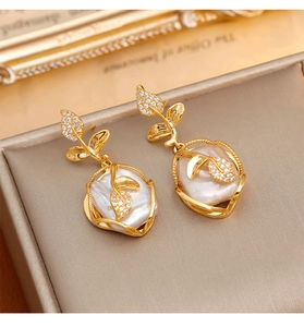 Detalle de pendientes de hoja dorada con perlas barrocas y circón sobre un joyero elegante