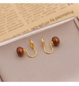 Détail de boucles d'oreilles clips vintage avec perles rondes brunes sur fond de journal