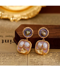 Dettaglio macro di orecchini di perle barocche con smalto viola e foglie d'oro