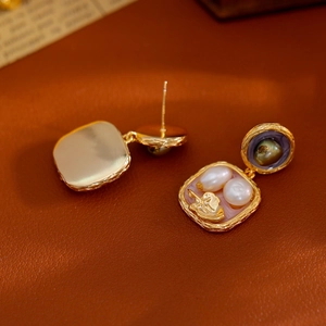 Orecchini di perle barocche con dettagli floreali dorati e smalto su sfondo in pelle vintage