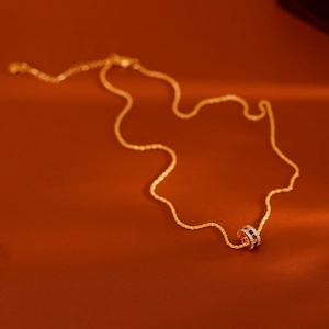 Elegante gouden ketting met cilindrische hanger voorzien van gekleurde zirkoonstenen op achtergrond