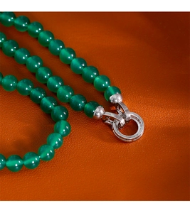 Détail macro de perles d'agate verte translucide avec un fermoir argenté sur cuir texturé