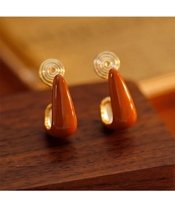 Macro shot of brown teardrop clip-on earrings with gold mosquito coil backs on wood