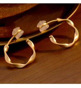 Détail macro de boucles d'oreilles clips torsadées dorées mates sur un plateau vintage