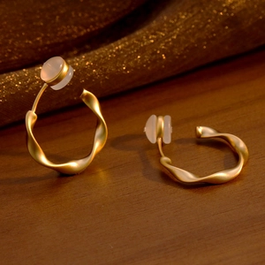 Boucles d'oreilles dorées torsadées minimalistes avec perles sur fond de texture boisée