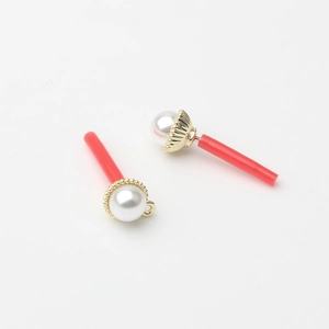 Detail of faux pearl earring pendant with gold metal base and long red cylinder drop