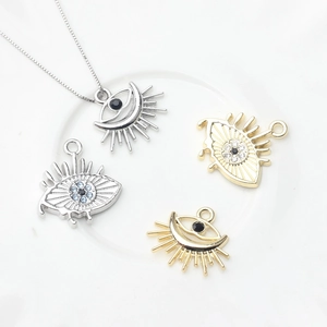 Gold and silver Evil Eye charms with blue zircon inlay on white background
