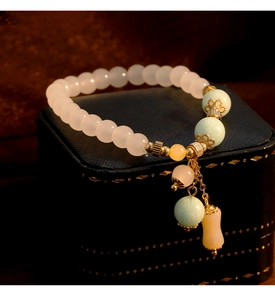Primer plano macro de pulsera de piedras naturales con dijes dorados en estuche de joyería