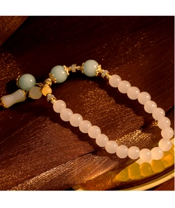 Detalle de pulsera de piedra natural blanca con cuentas verdes sobre tela de seda oscura