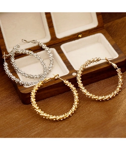 Gros plan de créoles texturées dorées et argentées dans un écrin à bijoux en bois